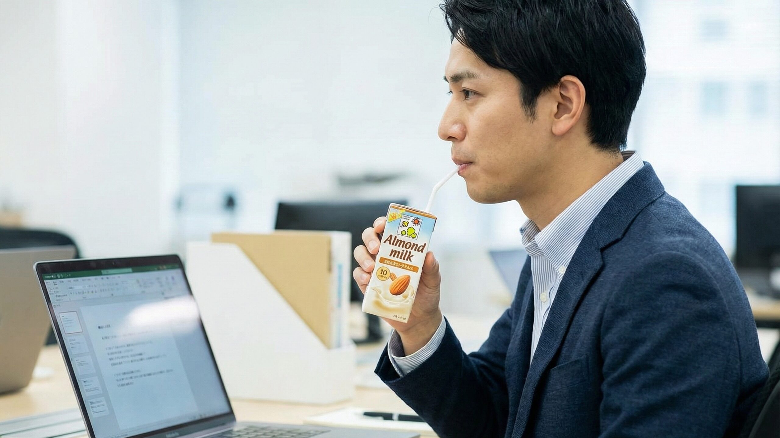 デスクワークの合間に、手軽に食物繊維を摂取できるアーモンドミルクを飲んで一息つくビジネスマン。