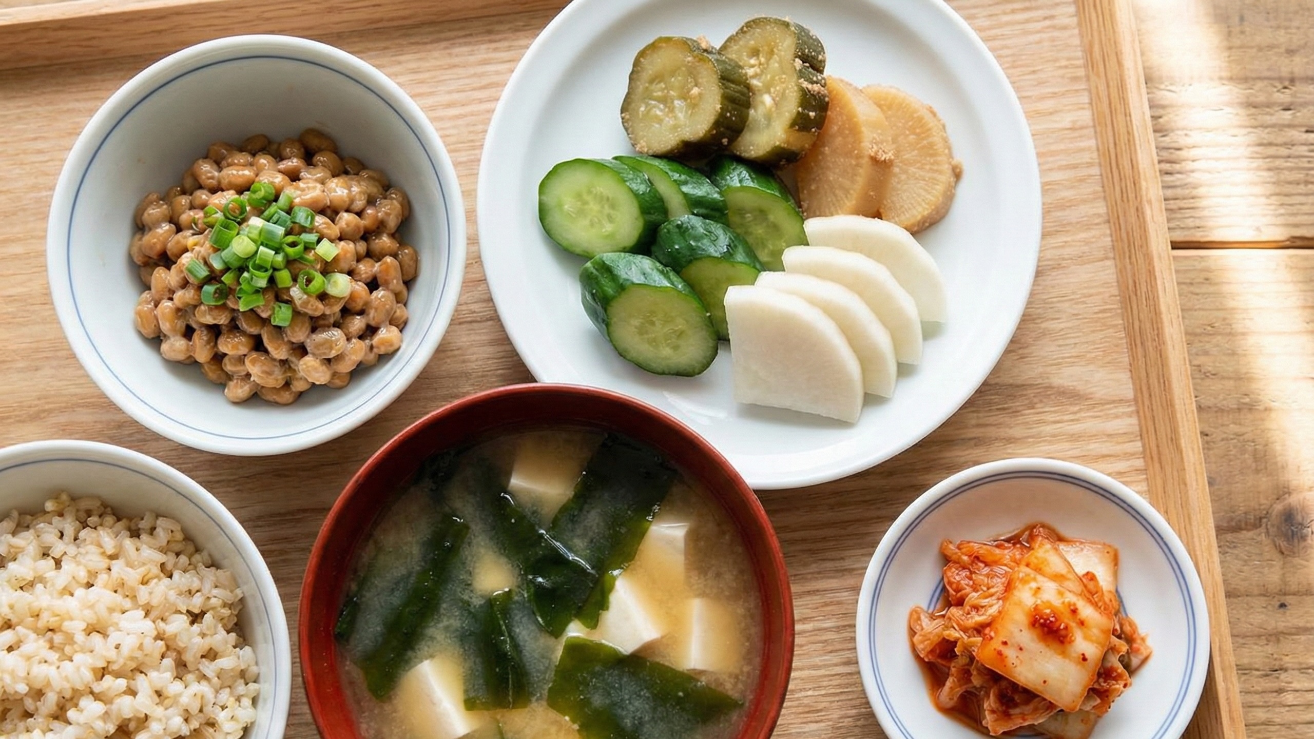 玄米、わかめの味噌汁、納豆、漬物、キムチが小皿に盛られて並ぶ健康的な朝食。