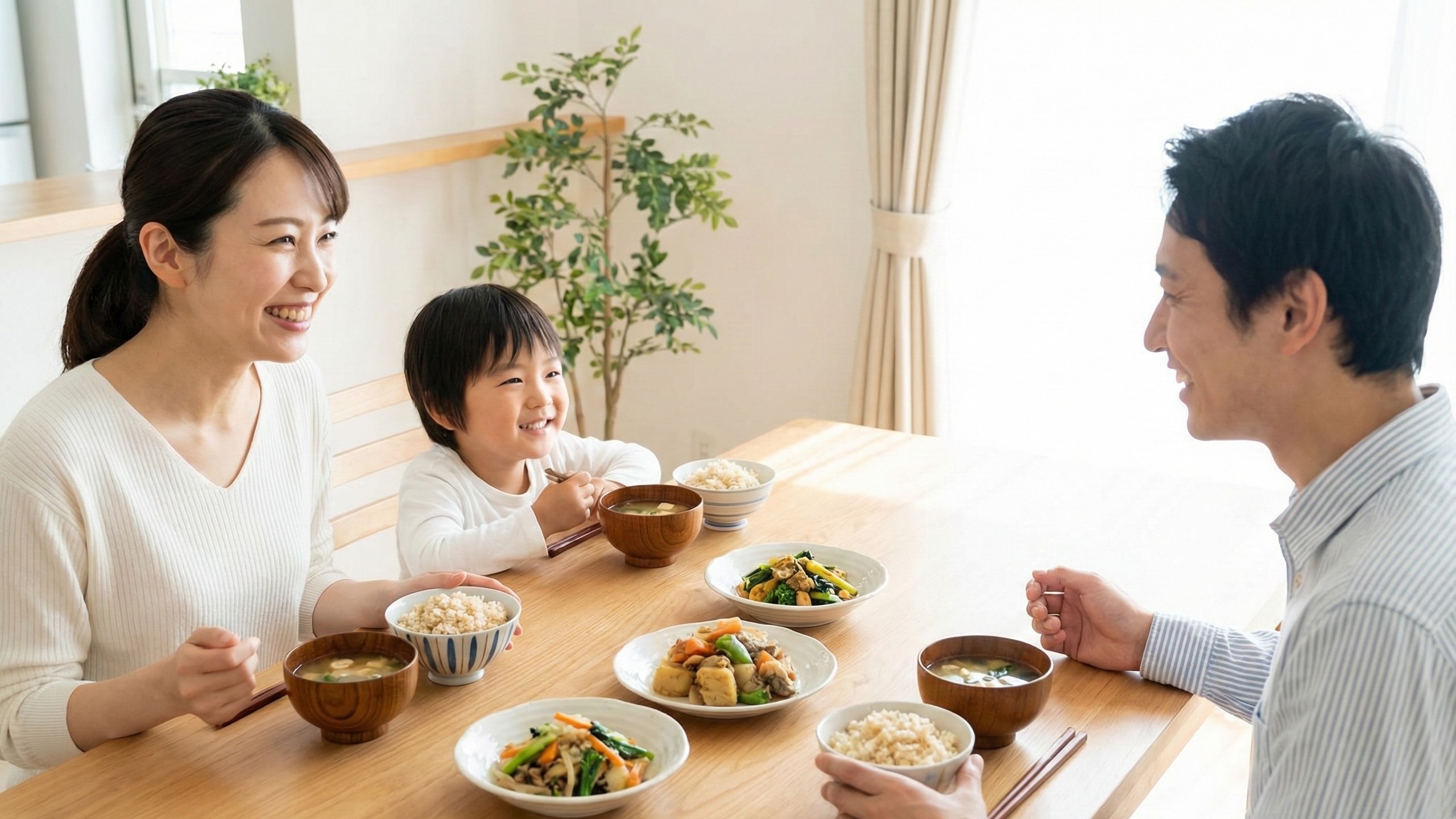 LPSを含む玄米や旬の野菜料理を囲んで笑顔で食事をする3人家族。健康的な食生活と、注目の成分LPSを摂取する日々の食卓。