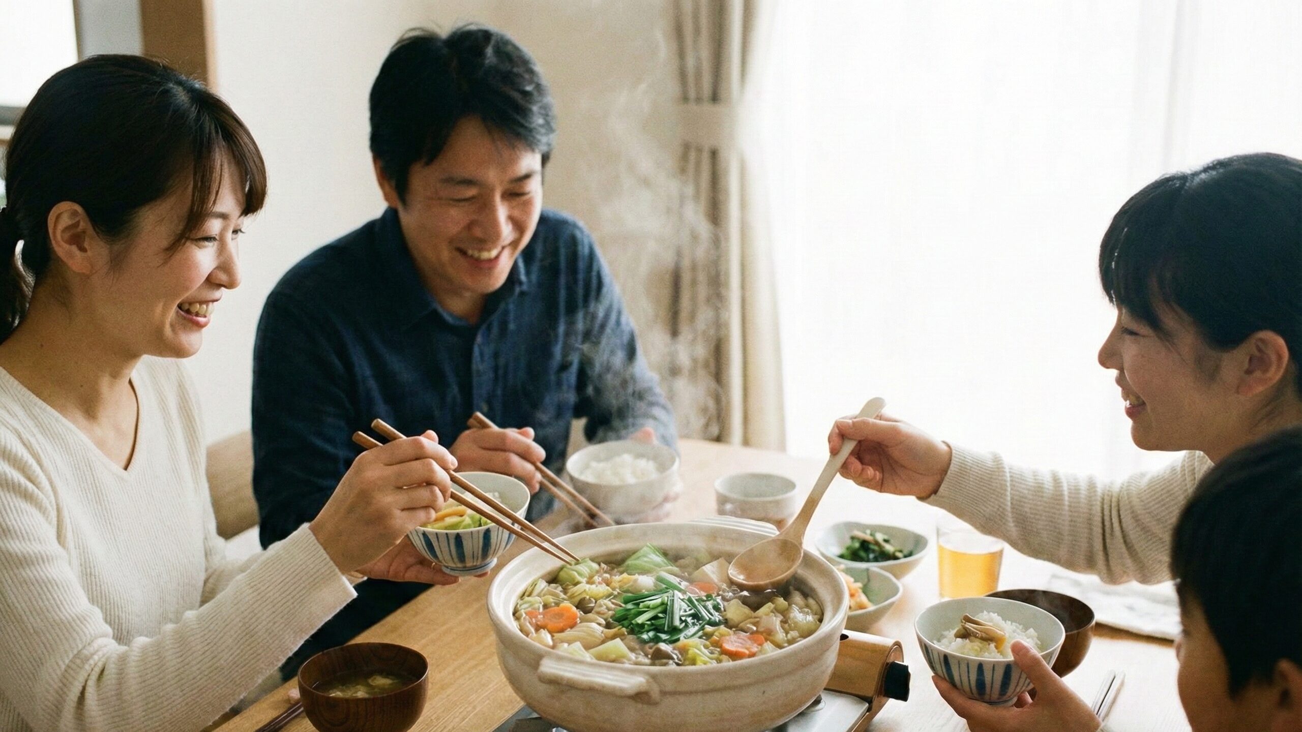 湯気が立ち上る大きな土鍋を囲み、笑顔で会話を楽しみながら食事をする4人の家族