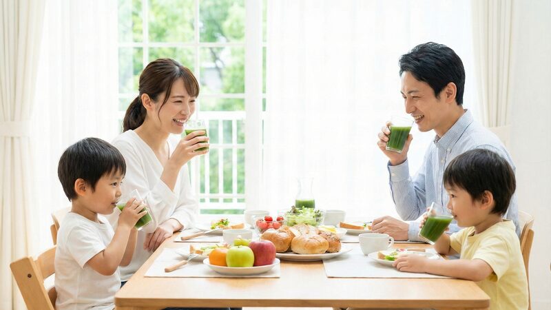 家族みんなの栄養管理。朝食の時間に笑顔で青汁を飲み、葉酸不足を補う親子4人の食事風景。