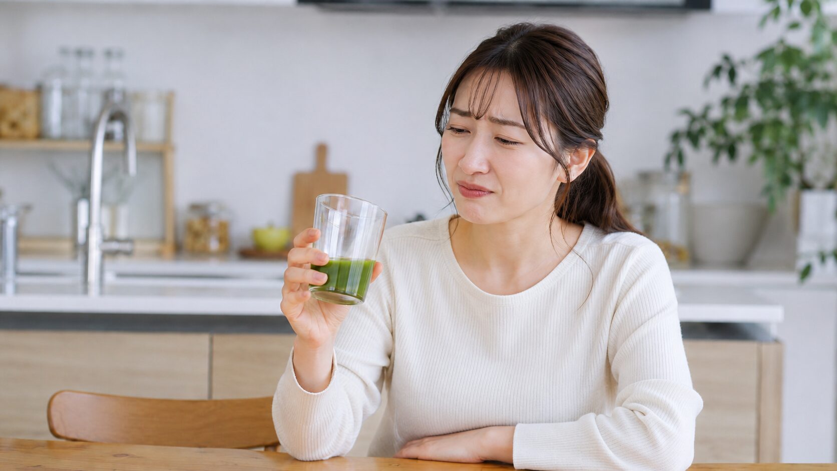 青汁特有の苦味や独特な味に、苦笑いのような困り顔を見せる女性。飲みにくさのイメージ。